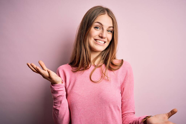 Joven hermosa pelirroja vistiendo suéter casual sobre fondo rosa aislado sonriendo alegre con los brazos abiertos como bienvenida amistosa, saludos positivos y seguros
 - Foto, imagen