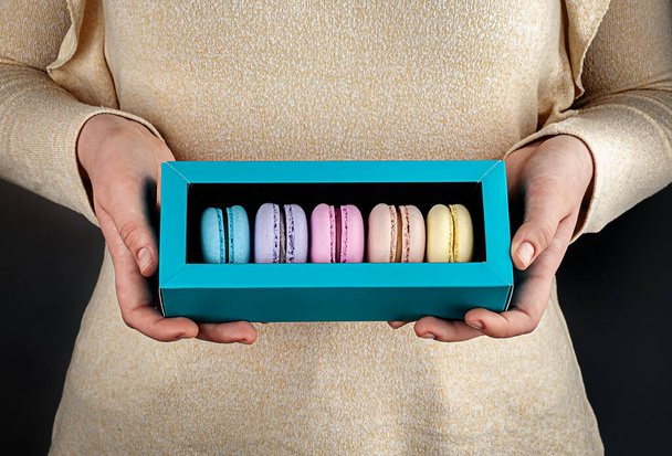 Two beautiful female hands are holding multicolored french macaroons in gift box - Foto, Imagem