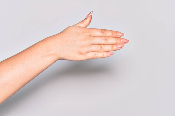 Mano de mujer joven caucásica estirándose y alcanzando con la mano abierta para el apretón de manos, mostrando la parte posterior de la mano - Foto, imagen