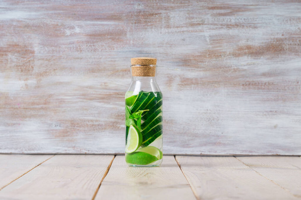 Detox Infused Water met komkommer, limoen en munt in Sports Bottle, met gesneden stukken komkommer en limoen in de buurt - Foto, afbeelding