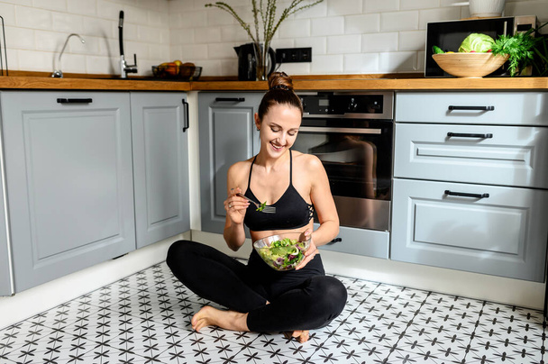 Young woman eats salat in the kitchen - Photo, Image