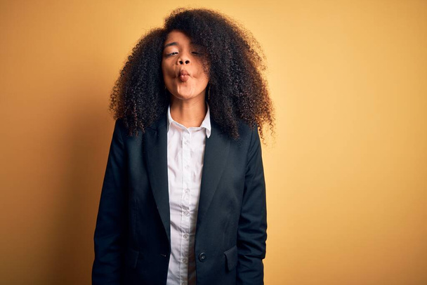 Young beautiful african american business woman with afro hair wearing elegant jacket making fish face with lips, crazy and comical gesture. Funny expression. - Фото, зображення