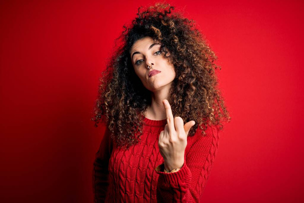Young beautiful woman with curly hair and piercing wearing casual red sweater Showing middle finger, impolite and rude fuck off expression - Fotó, kép