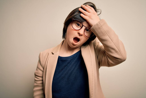 Mladý dolů syndrom obchodní žena nosí brýle stojící nad izolovaným pozadím překvapen s rukou na hlavě omylem, nezapomeňte chybu. Zapomenutá, špatná koncepce paměti. - Fotografie, Obrázek