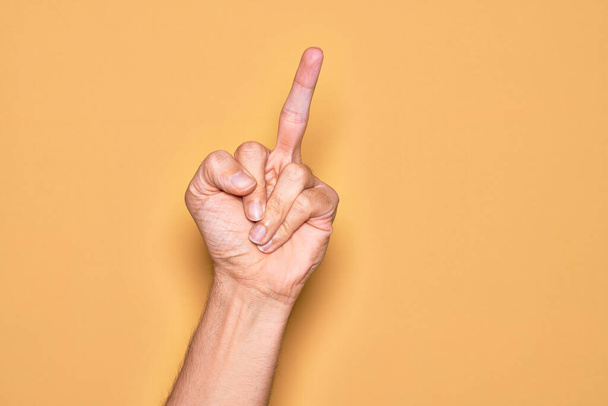 Рука кавказького молодого чоловіка, що показує пальці над ізольованим жовтим тлом, показує провокаційний і грубий жест, роблячи хуй, ви символ середнім пальцем
 - Фото, зображення