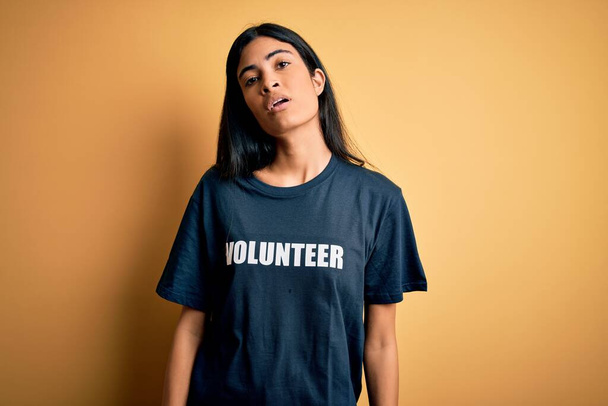Jovem bela mulher hispânica vestindo camiseta voluntária como caridade social moral olhando sonolento e cansado, exausto por fadiga e ressaca, olhos preguiçosos pela manhã
. - Foto, Imagem
