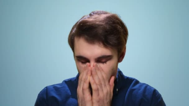 Sick man sneezing in studio. Close up ill guy sneezing on blue background - Filmati, video