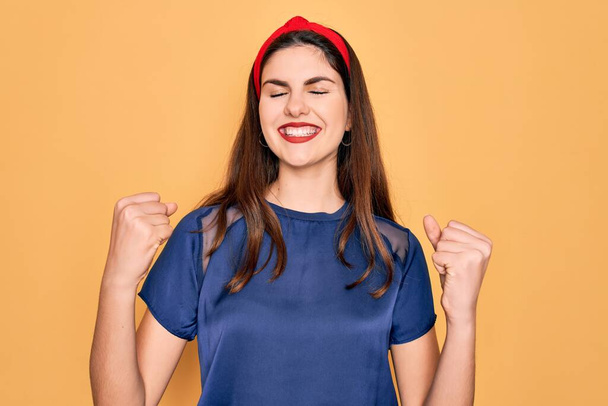 Young beautiful brunette woman wearing red lips over yellow background excited for success with arms raised and eyes closed celebrating victory smiling. Winner concept. - Fotoğraf, Görsel
