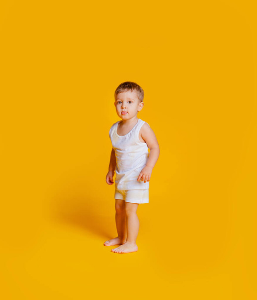 jongen staat in een wit T-shirt en onderbroek op een oranje-gele achtergrond - Foto, afbeelding