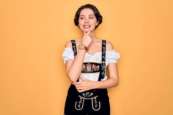 青い目の若い美しいドイツ人女性は、質問について考える顎に手で伝統的な10月祭のドレスを着て、包括的な表現。思慮深い顔で微笑んだ。疑いの概念. - 写真・画像
