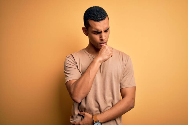 Young handsome african american man wearing casual t-shirt standing over yellow background feeling unwell and coughing as symptom for cold or bronchitis. Health care concept. - Fotografie, Obrázek