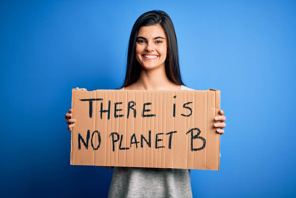 Giovane bella donna bruna attivista che tiene uno striscione per protestare per prendersi cura del pianeta con un viso felice in piedi e sorridente con un sorriso fiducioso che mostra i denti
 - Foto, immagini