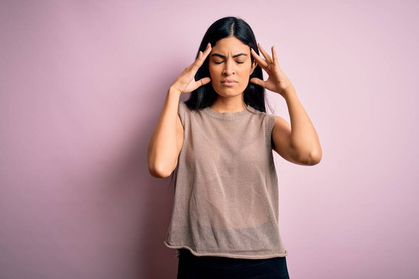 Young beautiful hispanic fashion woman wearing sweater over pink background suffering from headache desperate and stressed because pain and migraine. Hands on head. - Fotoğraf, Görsel