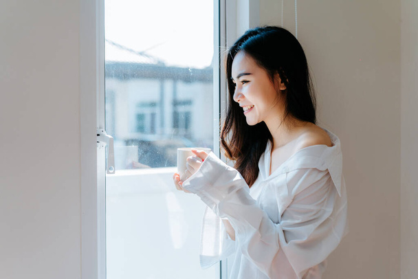 Asijské žena pití kávy v ranní snídani v okně ložnice čerstvý start den štěstí relaxovat doma zdravý životní styl  - Fotografie, Obrázek