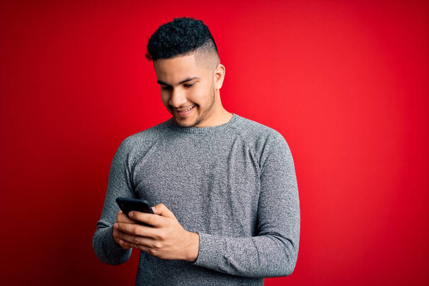 Молодой красивый мужчина разговаривает с помощью смартфона на красном фоне со счастливым лицом стоя и улыбаясь с уверенной улыбкой показывая зубы
 - Фото, изображение