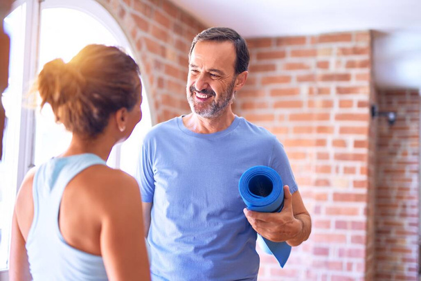 Middle age beautiful sporty couple smiling happy. Standing with smile on face holding mat and speaking at gym - Photo, Image