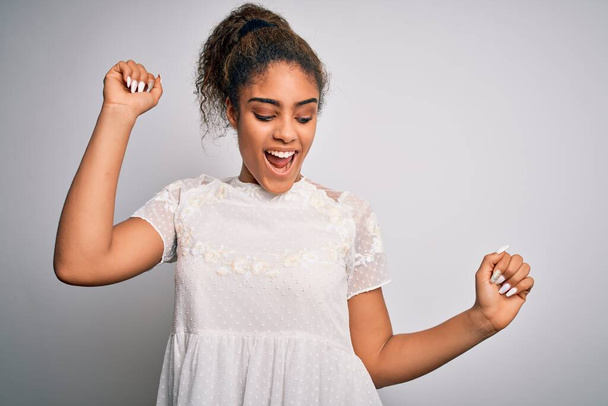 Young beautiful african american girl wearing casual t-shirt standing over white background Dancing happy and cheerful, smiling moving casual and confident listening to music - Foto, Imagem