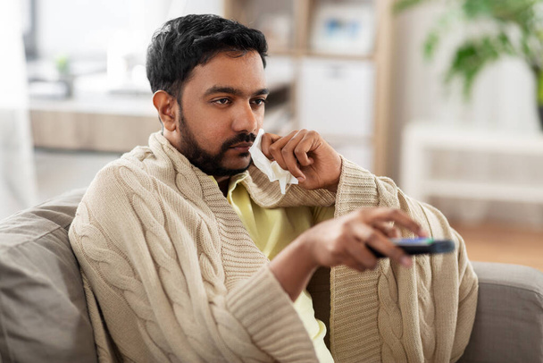 sick man with paper tissue and tv remote at home - Foto, Imagen