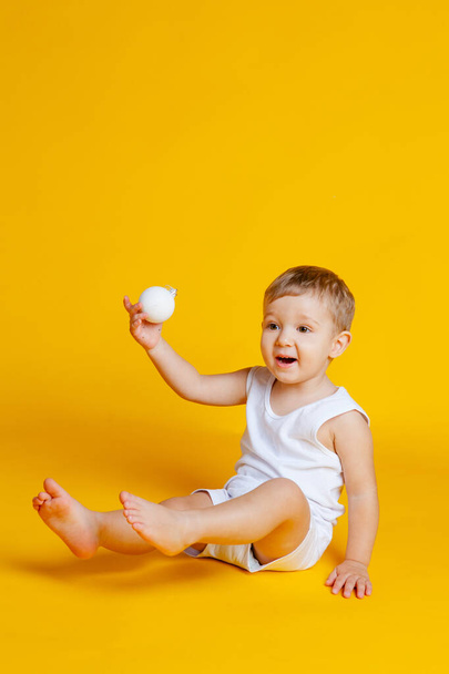 garçon en t-shirt et culotte sur un fond jaune orangé avec une boule de Noël blanche à la main
 - Photo, image