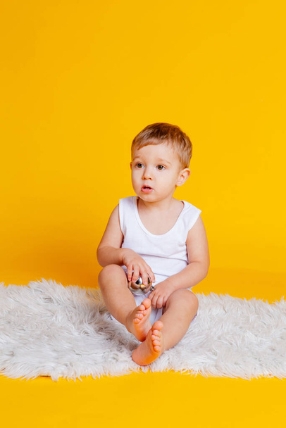 chlapec v tričku a spodky na oranžovo-žlutém pozadí s vánoční míč v ruce - Fotografie, Obrázek