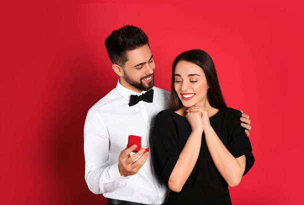 Man with engagement ring making marriage proposal to girlfriend on red background - Photo, image