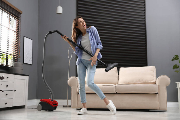 Young woman having fun while vacuuming at home - Foto, afbeelding