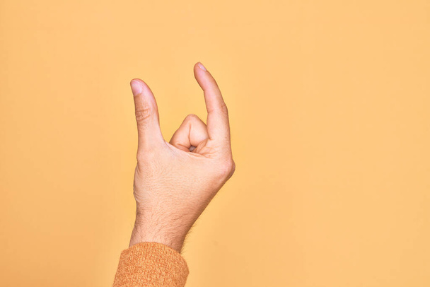 Mano de joven caucásico mostrando los dedos sobre el fondo amarillo aislado recogiendo y tomando cosa invisible, sosteniendo el objeto con los dedos mostrando el espacio - Foto, Imagen