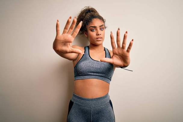 Молодая африканская американская спортсменка, занимающаяся спортом в спортивной одежде на белом фоне делает рамку с помощью ладоней и пальцев, камеры перспективы
 - Фото, изображение