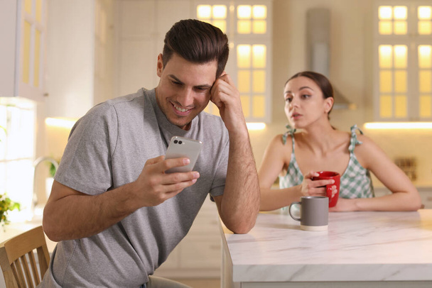 Distrustful woman peering into boyfriend's smartphone at home. Jealousy in relationship - Zdjęcie, obraz