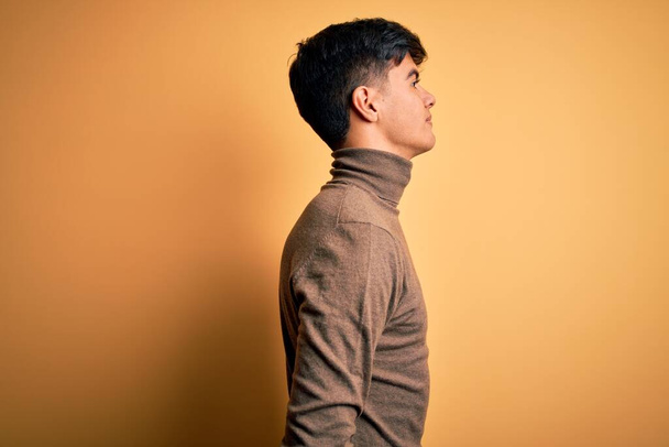Young handsome man wearing casual turtleneck sweater over isolated yellow background looking to side, relax profile pose with natural face with confident smile. - Фото, изображение
