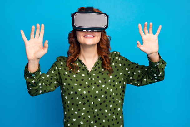 Photo of pretty crazy lady raise hands watch space galaxy planets show in vr box goggles try to touch cosmic ship wear green dotted shirt isolated blue color background - Foto, Imagem