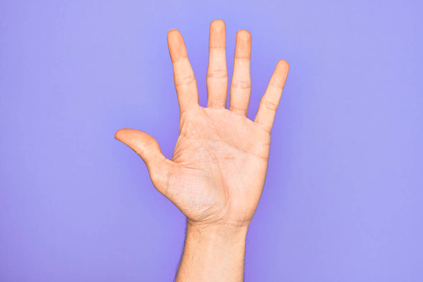 Рука кавказького молодого чоловіка, що показує пальці над ізольованим фіолетовим тлом підрахунок числа 5 показує п'ять пальців
 - Фото, зображення