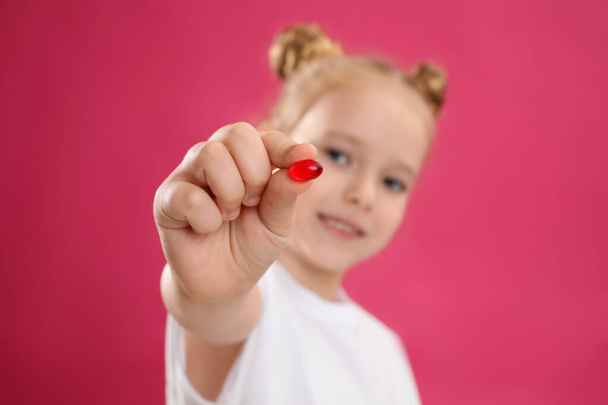 Little girl with vitamin pill against pink background, focus on hand - Fotoğraf, Görsel