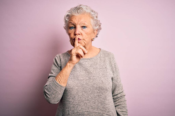 Senior mooie vrouw draagt casual t-shirt staan over geïsoleerde roze achtergrond vragen om stil te zijn met de vinger op de lippen. Stilte en geheim concept. - Foto, afbeelding