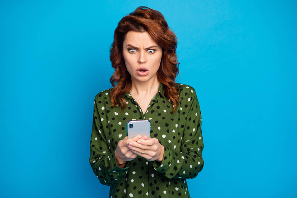 Photo of attractive pretty mad lady telephone hands open mouth check blog followers read negative comments reaction wear green dotted shirt isolated blue color background - Фото, зображення