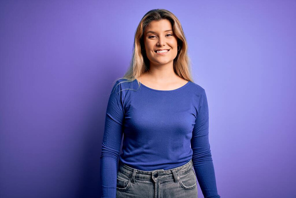 Young beautiful blonde woman wearing casual t-shirt over isolated purple background with a happy and cool smile on face. Lucky person. - Foto, Imagem