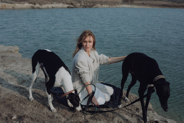 Жінка на прогулянці з собаками. Жінка сидить на озері з собаками
 - Фото, зображення