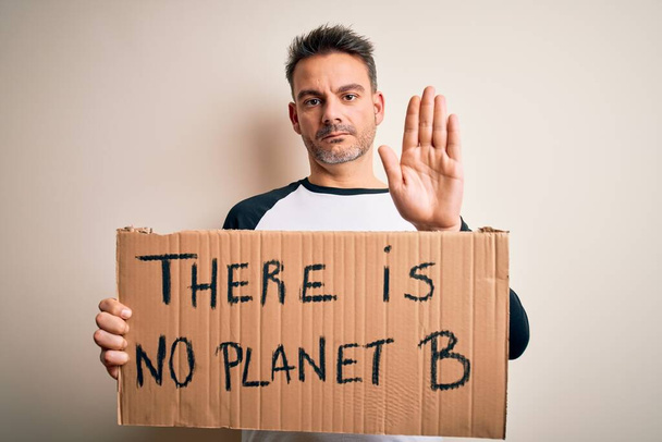 Jeune homme beau demandant l'environnement tenant la bannière avec le message de planète avec la main ouverte faisant stop signe avec l'expression sérieuse et confiante, geste de défense
 - Photo, image