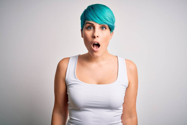 Νεαρή όμορφη γυναίκα με μπλε μαλλιά μόδας φορώντας casual t-shirt πάνω από λευκό φόντο φοβισμένος και σοκαρισμένος με έκπληξη και κατάπληκτος έκφραση, φόβο και ενθουσιασμένος πρόσωπο. - Φωτογραφία, εικόνα