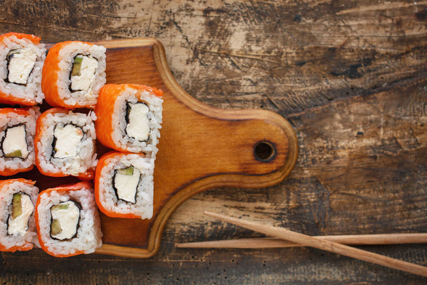Rollo de sushi con salmón, aguacate y queso sobre tabla de madera sobre fondo rústico. - Foto, imagen