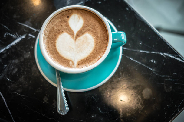 eten achtergrond mooie koffie kopje met latte kunst geplaatst op marmeren tafel door kantoor in de ochtend - Foto, afbeelding