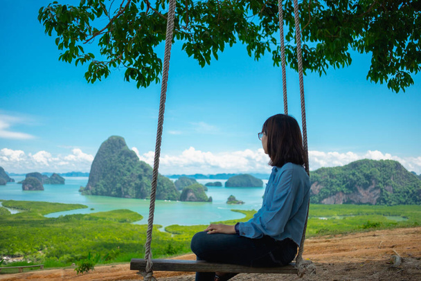 sceneria tło młoda kobieta siedzi sama na huśtawce pod drzewem na wyspie z morzem  - Zdjęcie, obraz