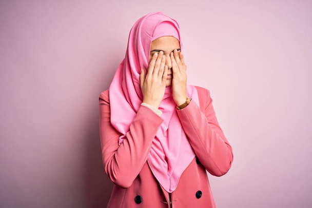 Nuori kaunis tyttö yllään muslimi hijab seisoo yli eristetty vaaleanpunainen tausta hankaus silmät väsymys ja päänsärky, unelias ja väsynyt ilme. Näköhäiriö
 - Valokuva, kuva