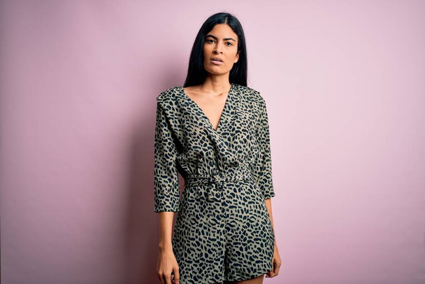 Young beautiful hispanic fashion woman wearing casual dress over pink background with serious expression on face. Simple and natural looking at the camera. - Φωτογραφία, εικόνα