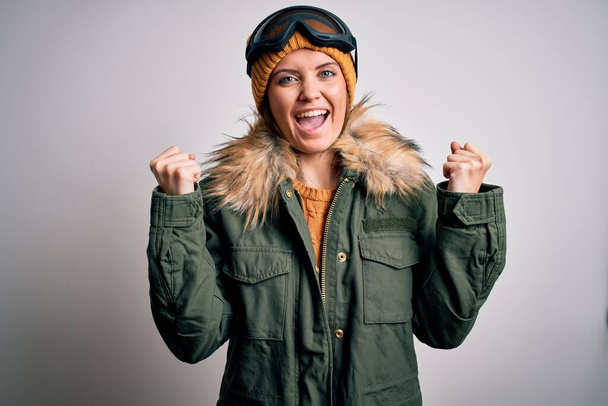 Молодая красивая лыжница с голубыми глазами, в снежной спортивной одежде и лыжных очках, радовалась и удивлялась успеху с поднятыми руками и открытыми глазами. Концепция победителя
. - Фото, изображение