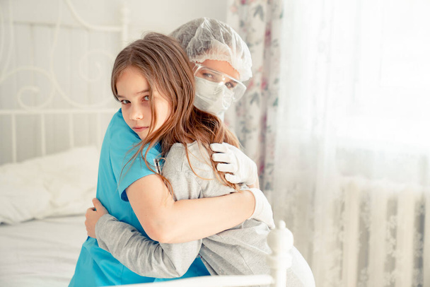 Γιατρός με μάσκα εξετάζει παιδί στο σπίτι και αγκαλιάζει. - Φωτογραφία, εικόνα