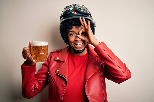 Jeune afro afro-américaine femme motocycliste avec les cheveux bouclés boire pot de bière avec le visage heureux souriant faire ok signe avec la main sur les yeux en regardant à travers les doigts
 - Photo, image