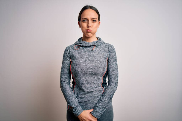 Fiatal szőke fitness nő visel sport edzőruha felett elszigetelt háttér puffadt arc vicces arc. Száj felfújt levegővel, őrült kifejezés. - Fotó, kép