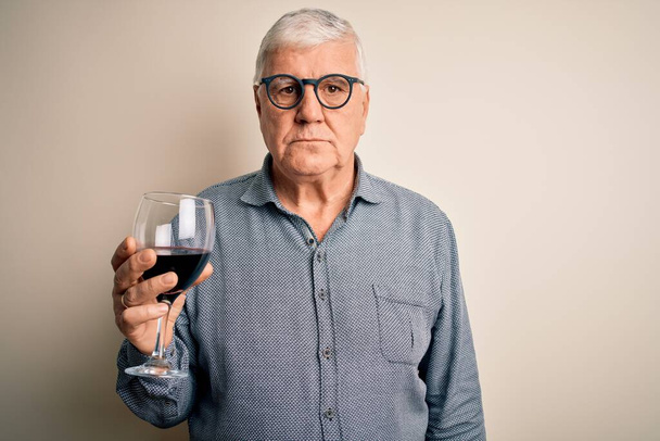 Senior bonito hoary homem beber copo de vinho tinto sobre fundo branco isolado com uma expressão confiante no rosto inteligente pensando sério
 - Foto, Imagem