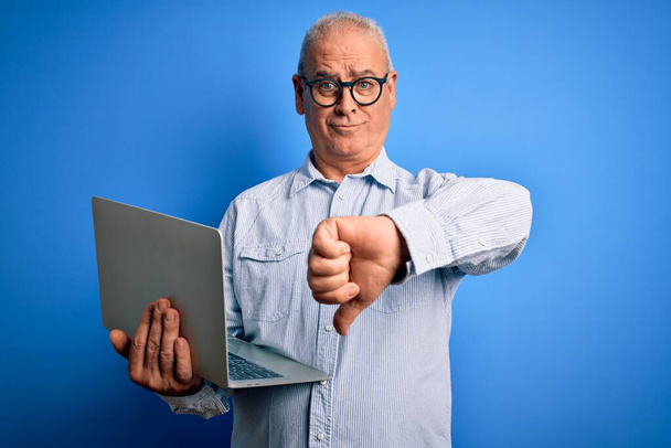 Красивий діловий чоловік середнього віку в окулярах працює з використанням ноутбука з розлюченим обличчям, негативний знак, що показує нелюбов з великими пальцями вниз, концепція відторгнення
 - Фото, зображення